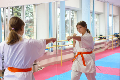 Sportive young girl wearing kimono doing exercises in large sports hall