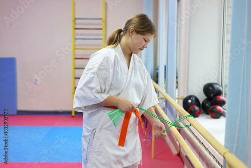 Sportive young girl wearing kimono doing exercises in large sports hall