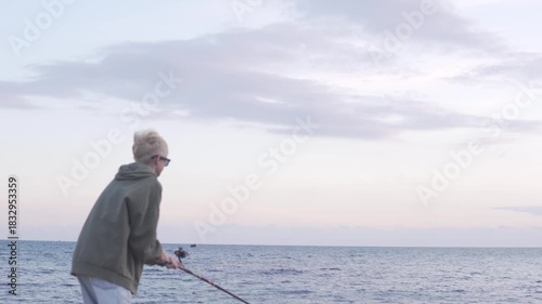 A blond boy fishes in the sea with a fishing rod.