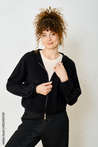 Young woman with curly hair wearing a stylish black hoodie in a bright indoor setting