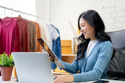 SME Startup: A young Asian woman working on a laptop and sending business emails to customers at home.