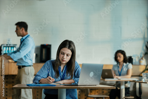 Female Student Taking Notes from Online Lecture in Sunny University Cafeteria During Lunch