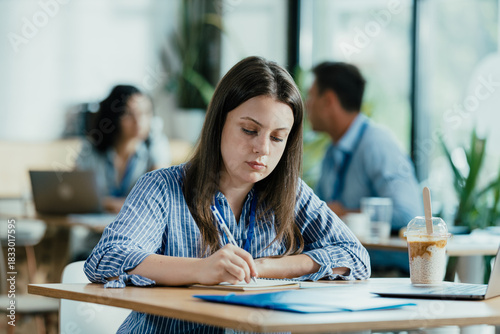 Female Student Taking Notes from Online Lecture in Sunny University Cafeteria During Lunch