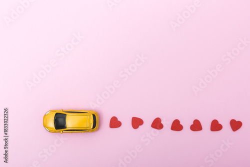 Wallpaper Mural Yellow toy car on a pink background, leaving a trail of red heart shapes, symbolizing love and affection in a playful and creative way, perfect for romantic themes Torontodigital.ca