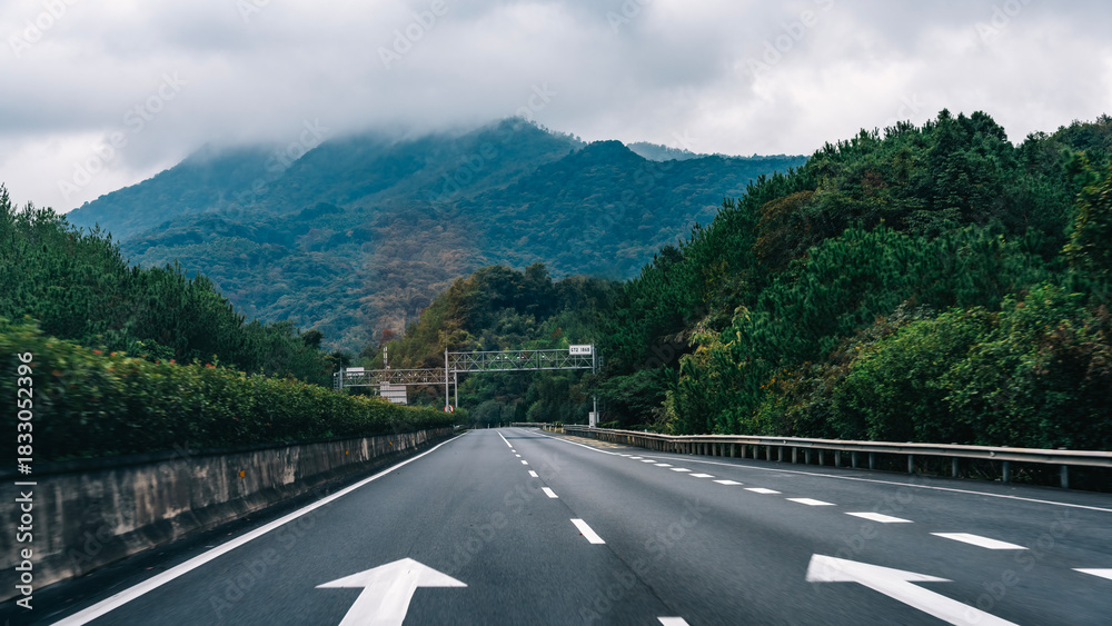 Fototapeta premium Scenic highway with arrows leading through lush greenery and mountains