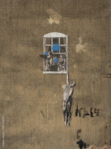 фотографія Stencil Street Art Mural: Hanging Man Reaching to a Window with Blue Paint Splat