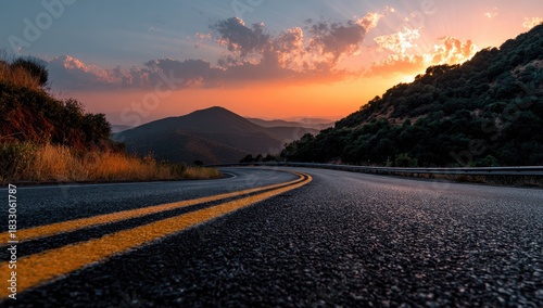 Asphalt road curves through mountain landscape under a vibrant sunset sky