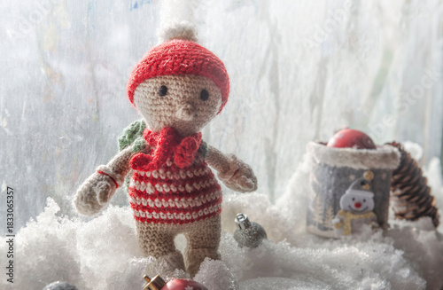 little handmade woolen figurine  with red  hat and scarf resting in the snow ...