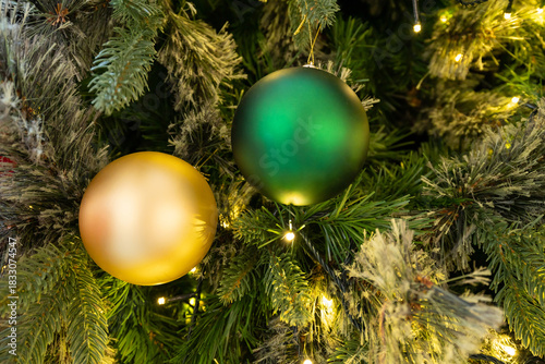 Vibrant green and gold baubles adorn a lush evergreen tree, illuminated by soft warm lights. A festive, cozy scene perfect for holiday decor, family gatherings, and seasonal celebrations.