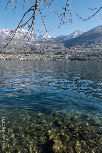 Crystal clear water along the shores of Lake Iseo near Montisola, with gentle ripples, rocky shallows, and soft light creating a peaceful lakeside scene in northern Italy.