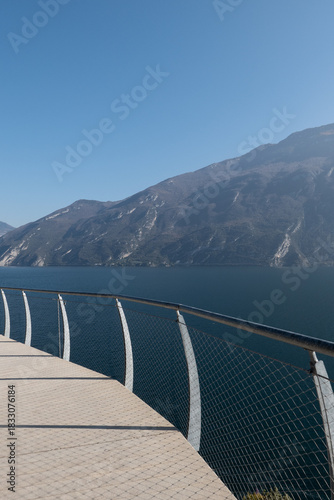Cliffside section of the Limone sul Garda cycle path, suspended above the lake with dramatic rock walls, blue water, and a sweeping panoramic view of the Garda landscape.