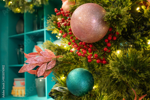 A lush Christmas tree sparkles with pink and teal baubles, red berries, and a poinsettia flower, creating a warm holiday centerpiece perfect for cozy home decor.