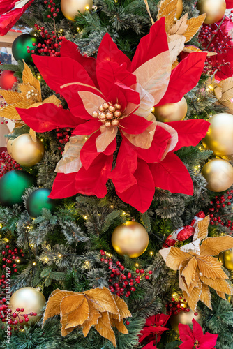 A lush Christmas tree adorned with bright red poinsettias, gold baubles, and shimmering leaves