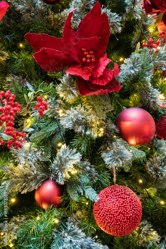 Lush Christmas tree adorned with red ornaments and a vivid poinsettia, illuminated by twinkling lights.