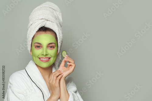 Smiling woman in green organic cosmetic face mask holding cucumber slices
