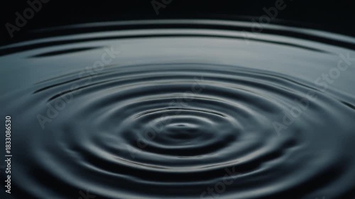 Ripples spreading across perfectly still black water as a single droplet falls