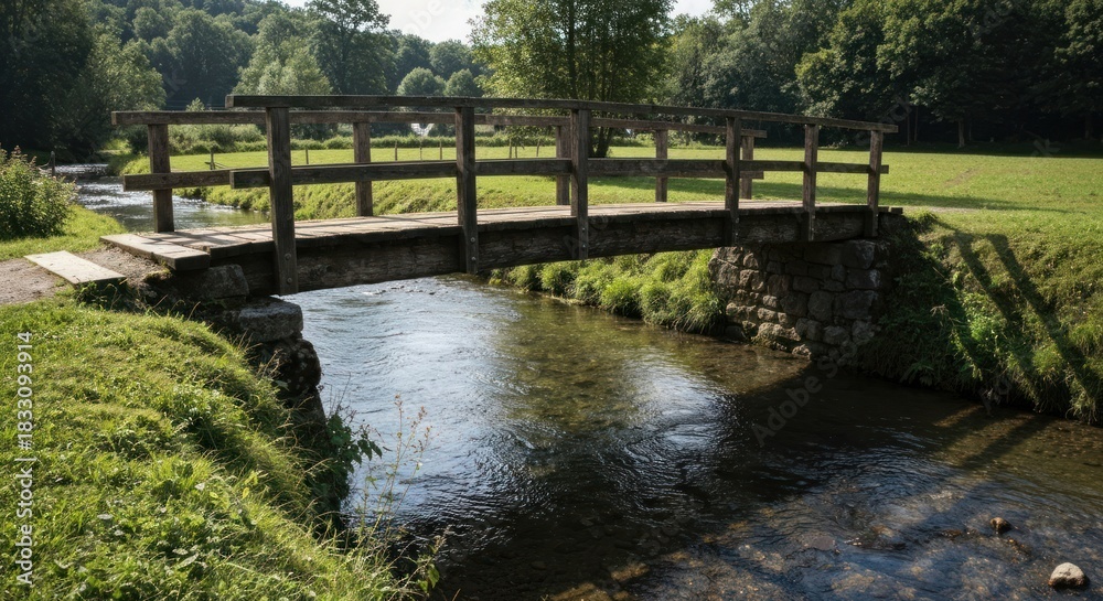 Fototapeta premium Wooden bridge spanning a small, clear stream in a verdant valley. Lush greenery surrounds the tranquil waterway