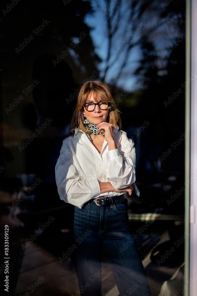 Fototapeta premium Portrait of a middle-aged blond haired woman standing behind the window