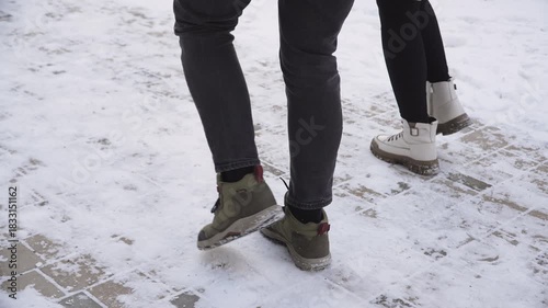 Legs of man and woman taking long, synchronized strides along snowy sidewalk. Cheerful couple enjoying winter walk in boots.