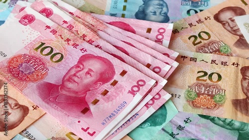 A wad of Chinese one hundred yuan (CNY) or renminbi (RMB) bills fall over table with heap of scattered notes of diffrent value. Saving money, financial income and growth, business concept.