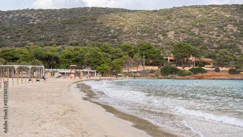 Fototapeta Naklejka Na Ścianę i Meble -  A red wooden lifeguard tower on the seashore in Greece against the backdrop of a bright blue sky and high mountains.