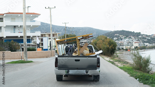 a large pickup truck, a junk dealer's vehicle, driving along a road in a village by the sea