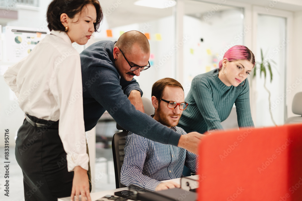 Fototapeta premium Team collaboration in a modern office with four businesspeople engaged in a project discussion around a computer in a bright workspace