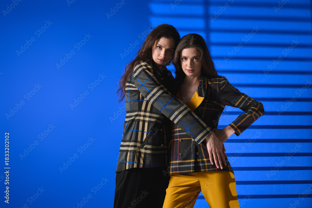 Naklejka premium Twins showcase stylish fashion with confidence in vibrant blue backdrop
