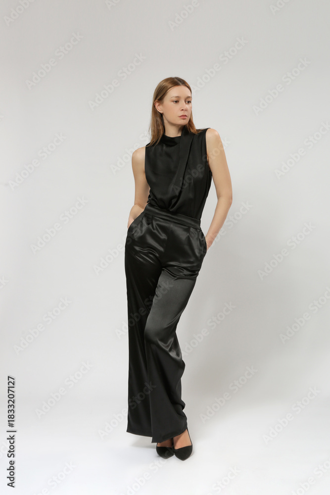 Fototapeta premium Female model wearing black blouse and wide satin black trousers. Classic and timeless simple fashion. Studio shot. 