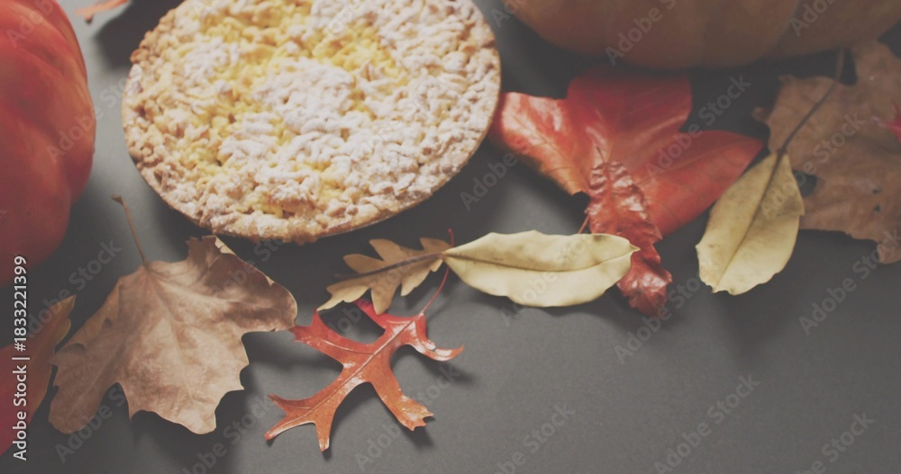 Naklejka premium Displaying small crumbed tart sitting on gray table at home, with dried autumn leaves and pumpkins