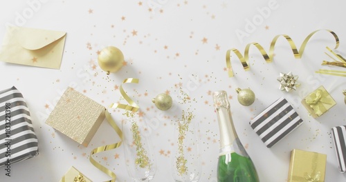 Displaying green champagne bottle and two flutes with gold glitter on white tabletop, curled ribbon