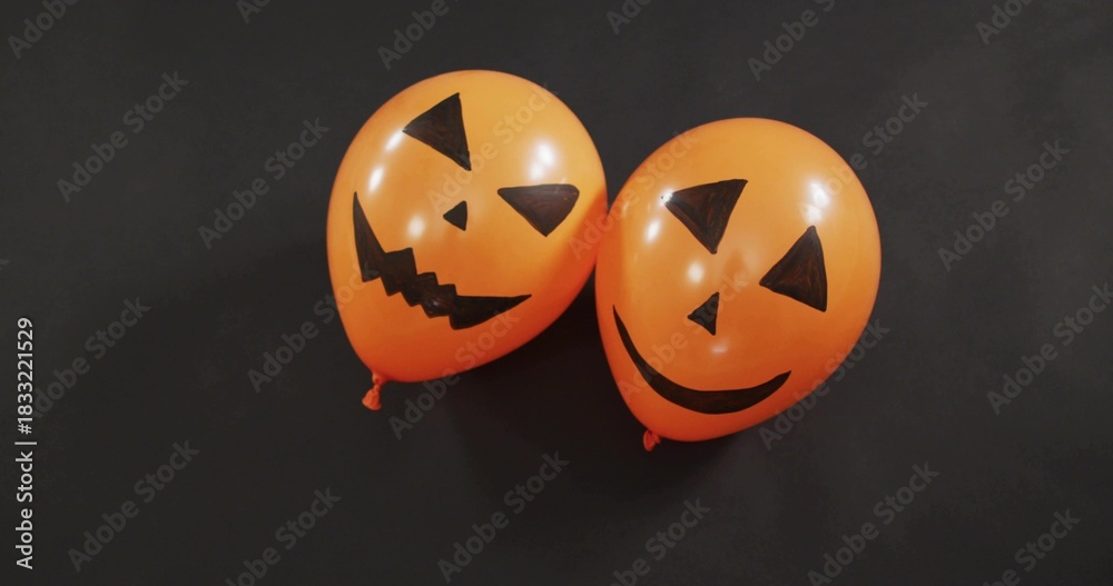 Fototapeta premium Displaying paired orange jack-o'-lantern balloons glowing under studio light, with knotted necks