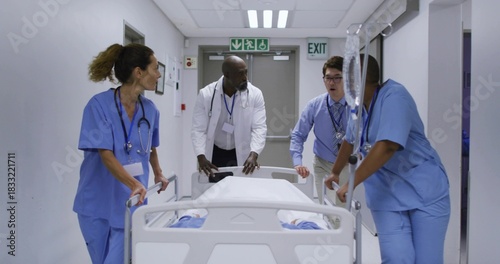 Pushing medical staff in scrubs and coat guiding covered gurney through ward, holding IV pole
