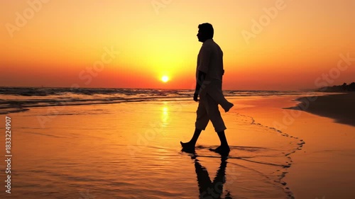 A solitary figure, silhouetted against a radiant sunset, walks along a tranquil beach. The water's edge reflects the warm glow of the sun