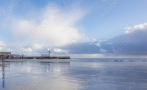 A beach and lighthouse where a receding tide has left ripples of water on the sand.