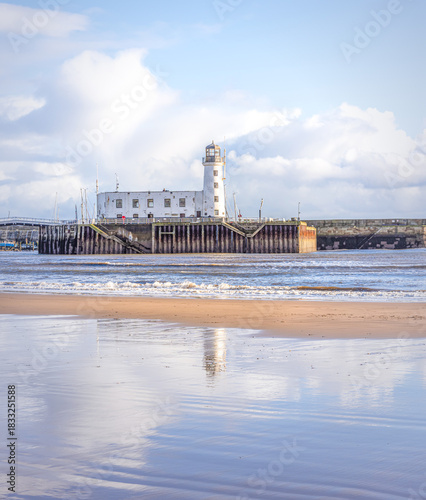 A beach and lighthouse where a receding tide has left ripples of water on the sand.