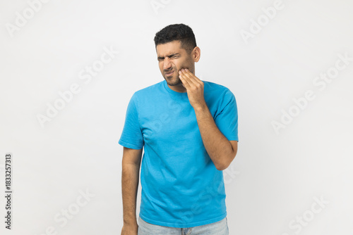 Sick unshaven man frowning his face, touching painful cheek, suffering terrible toothache.