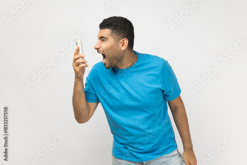 Angry despair man standing with mobile phone in hands, screaming while looking at cell phone.