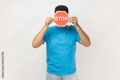 Unknown anonymous man standing hiding his face with behind red stop sign, prohibition.