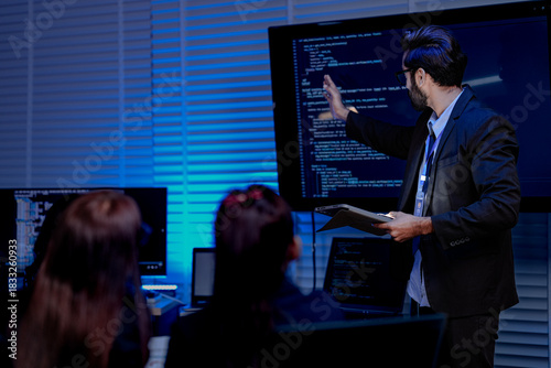 A focused male professional wearing glasses and a headset actively discusses a project gesturing with his hand in a modern blue lit office environment showcasing collaboration.