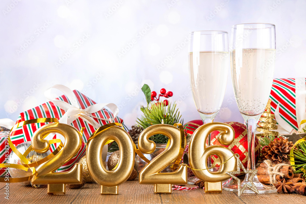 Obraz premium Festive Christmas and New Year 2026 background with champagne glasses, holiday baubles, Christmas tree decor, gift boxes
