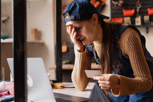 Anxious female repair shop owner facing online fraud issues while holding business credit card