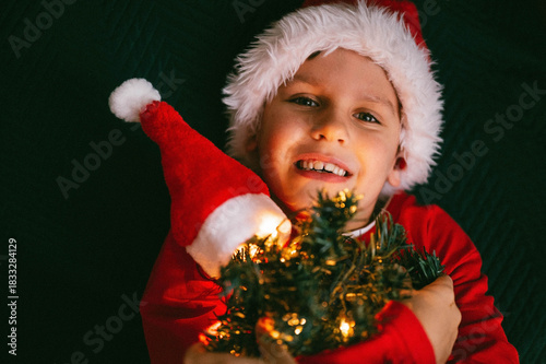 Merry Christmas and happy holidays. A cheerful boy with a small Christmas tree. The child is having fun on the bed.