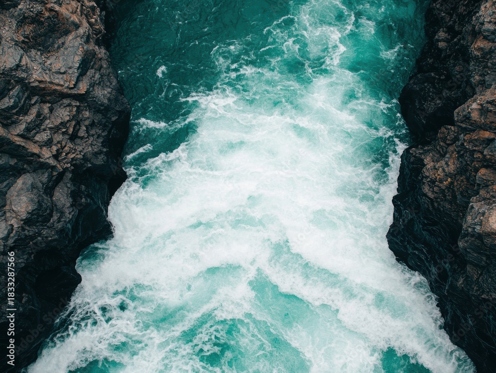 Obraz premium Aerial view of turquoise water crashing against dark rocky cliffs, creating a dynamic contrast between land and sea.