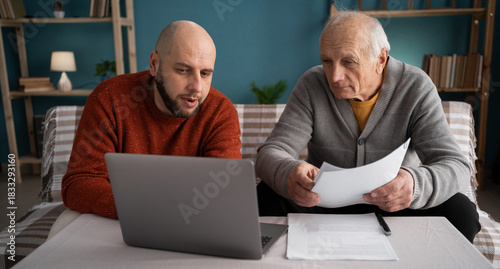 Adult son assisting senior retired father with online payments, mortgage loan, and form filling