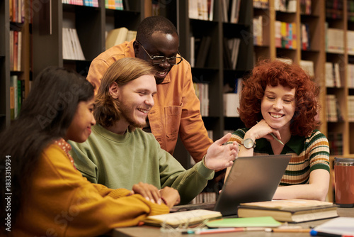 Foto Diverse group of young people collaborating around laptop in library, man gestur