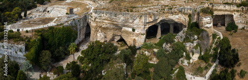 Panoramic aerial view of the Neapolis Archaeological Park, located in Syracuse, Sicily, Italy. It features the Ear of Dionysius, a limestone cave, the Grotta dei Cordari, and the Grotta del Salnitro. 