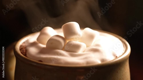 Warm hot chocolate with marshmallows, a hand reaching in, steaming drink