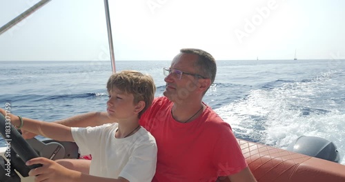 Little boy driving a speedboat under his father's supervision