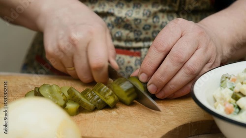 Hands cutting pickles on wooden board for traditional festive salad
